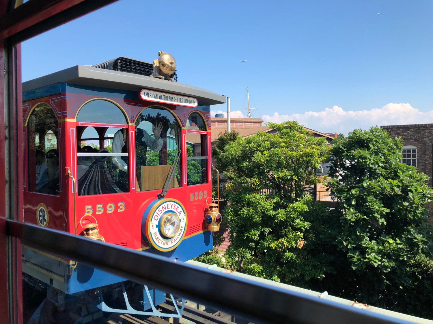 A conductor of a train on the Tokyo DisneySea Electric Railway waving to the camera as his train passes by an opposing train on the way to Port Discovery Station.